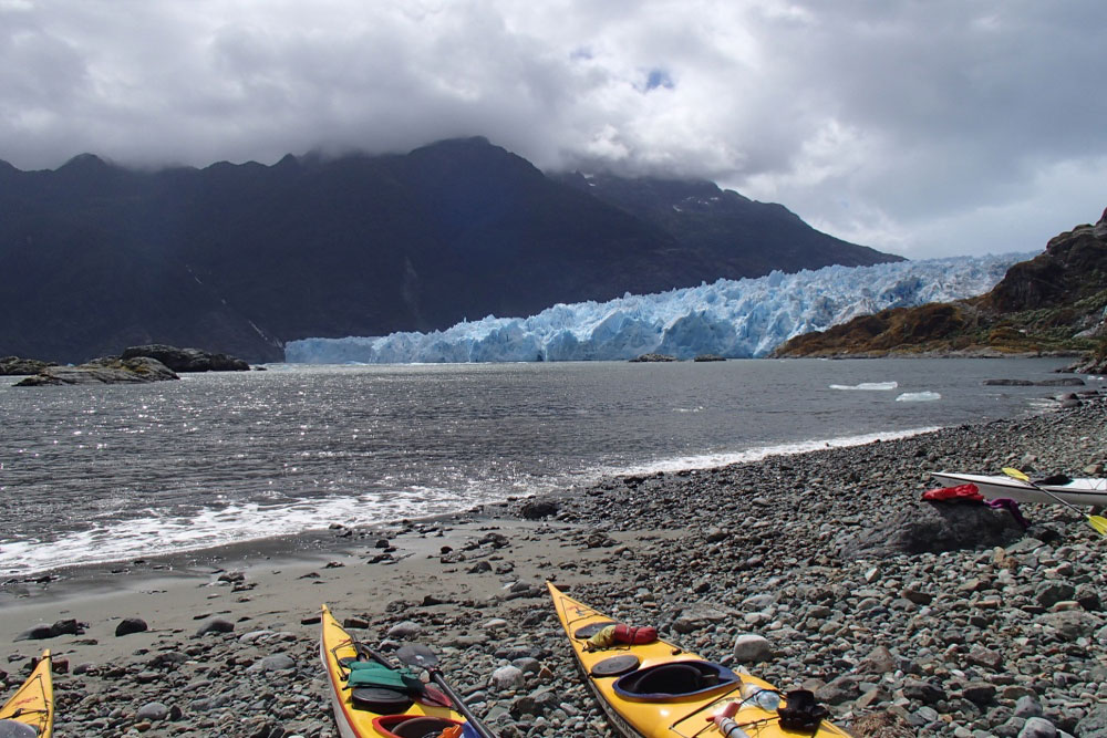 Kayaks on a beach across from a large glacier in Chile