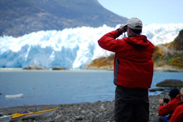 A person on a beach using binoculars to view the San Rafael Glacier from the shore