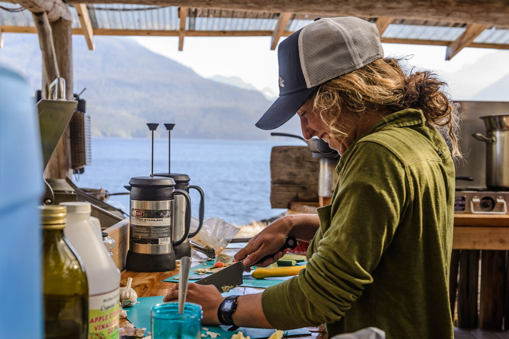 Guide preparing meal in outdoor kitchen at kayaking basecamp