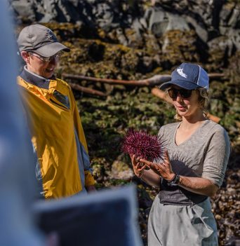 Guide explaining intertidal life to guest with a sea urchin