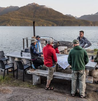 A group of people surrounding a marine chart on the shore of the Johnstone Strait