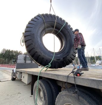 Excavator tire getting lifted onto a truck in Heriot Bay