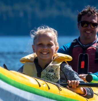 A young girl in a double kayak smiling