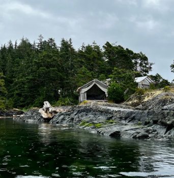 A kayaker paddling past a glamping tent in the Johnstone Strait