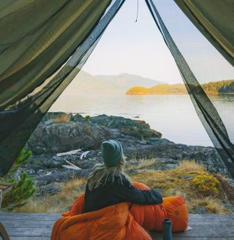 Camper enjoying the sunrise in an orange sleeping bag