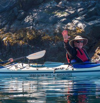 Kayaker waving in front of rocky cliff