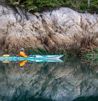 Kayaker resting along mirror-like water