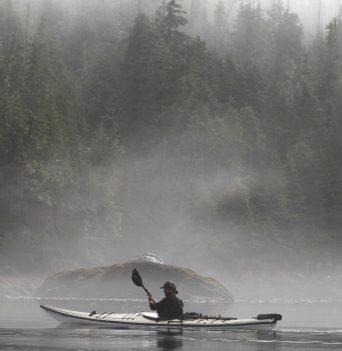 Man kayaking along foggy BC coast