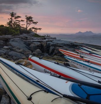 Kayaks docked on rocky shoal with the sunsetting in northern BC