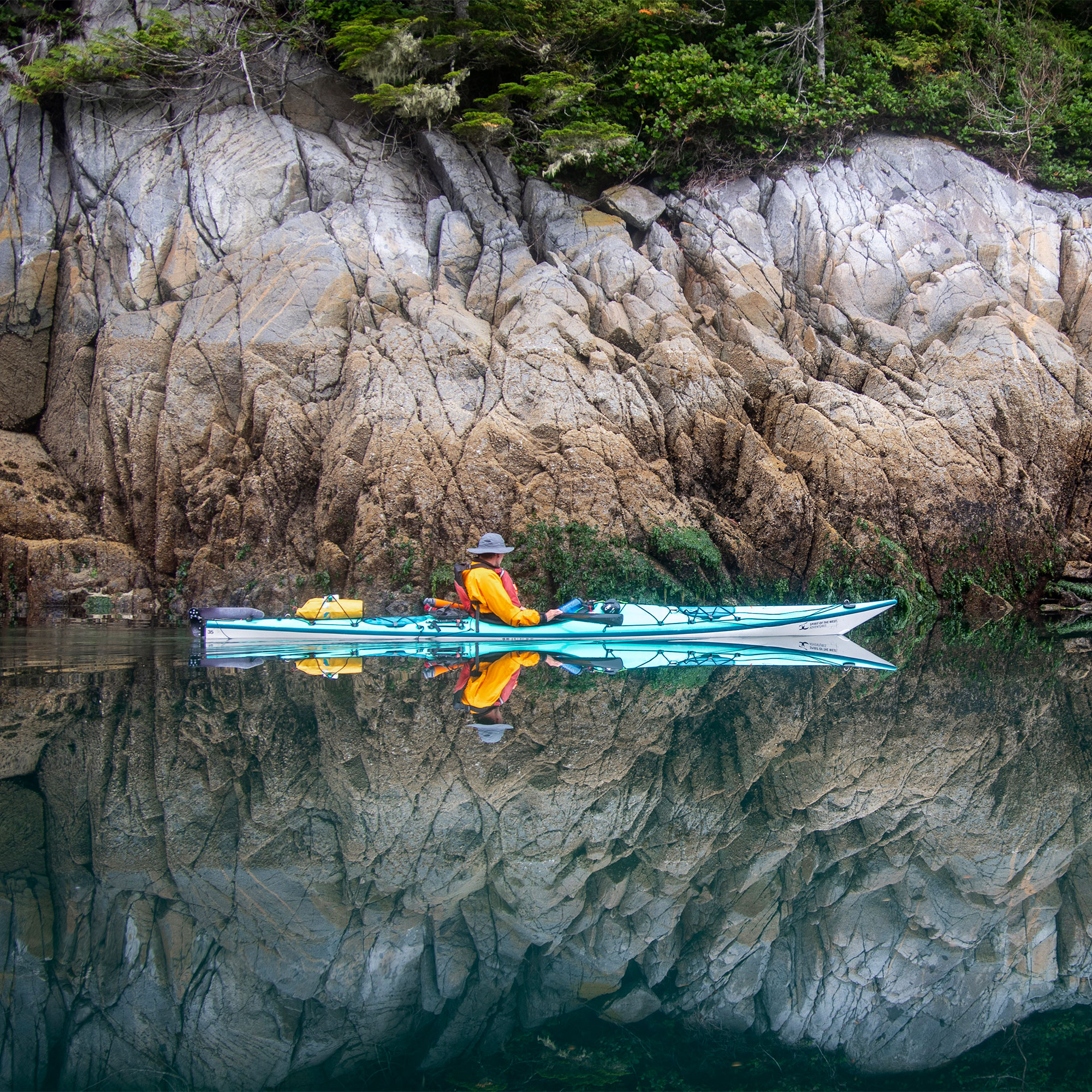 Person Kayaking in Wilderness Setting of Coastal BC with Rocky Tree-Lined Backdrop