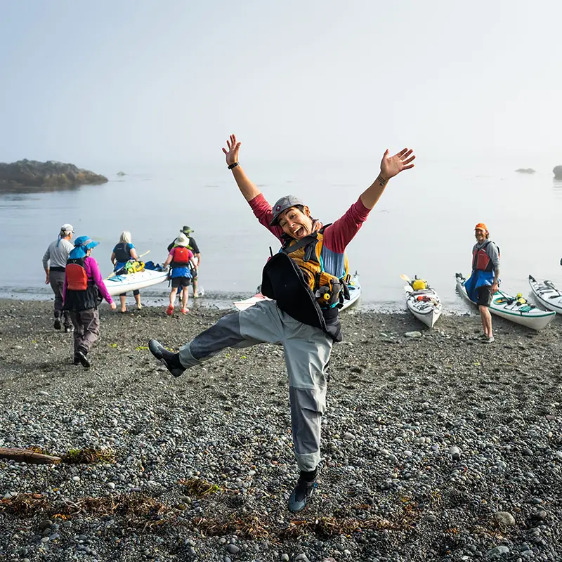 Happy Kayak Guide Jumping with Hands in Air with Coastal BC Backdrop