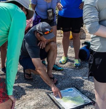 A person pointing at a chart on the ground while a group crowds around