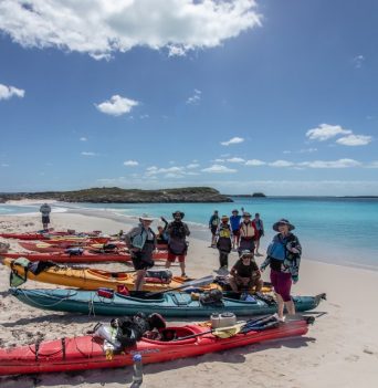 A group of people on a sandy beach standing next to colourful kayaks