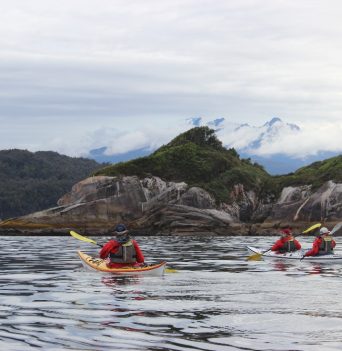 A group of kayakers paddling along the Chilean coastline
