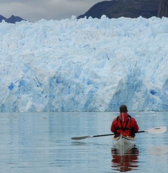 Kayaker resting in a kayak in front of a large Chilean glacier