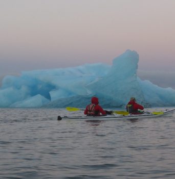 A double kayak paddling past a large iceberg in Chile