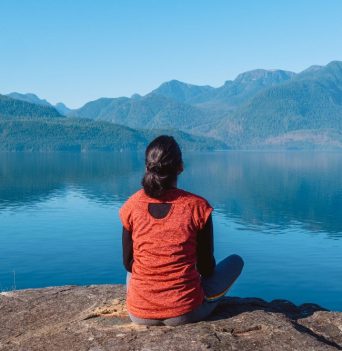A woman sitting on a rock looking at a calm ocean