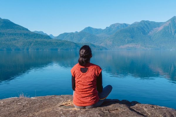 A woman sitting on a rock looking at a calm ocean