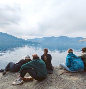 A group of people sitting on a cliffs edge watching wildlife in the distance