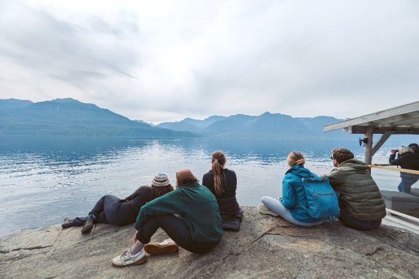 A group of people sitting on a cliffs edge watching wildlife in the distance