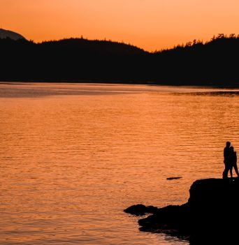 Two people under an orange sky watching the sunset over the ocean