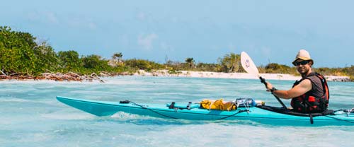 A kayaker in a blue kayak paddling in turquoise waters in the Bahamas