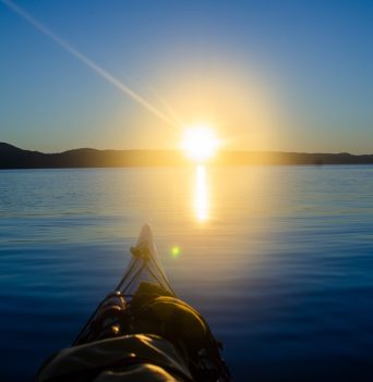 The nose of a kayak looking at the setting sun