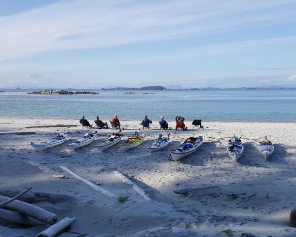 A white sandy beach with kayaks sitting on shore and a group of people sitting in chairs